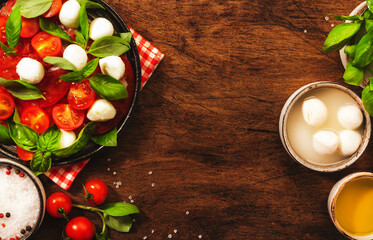Caprese - italian salad with red tomatoes and mozzarella cheese with green basil leaves. Top view, wooden table