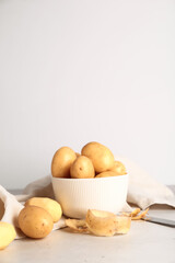 Bowl with raw potatoes on light background