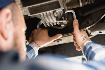 Obraz premium mechanic repairing bottom of lifted car with wrench on blurred 
