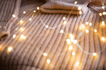 Fototapeta premium Lights of a luminous garland on a knitted sweater on the table. Background with soft focus. Christmas concept.