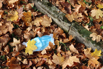 Waste during Covid-19. Medical protective face mask covered by autumn leaves in the park