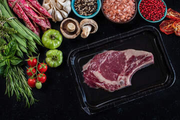 Raw beef meat in the vacuumed skin pack with vegetables on the rustic table