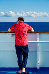 Man with bright shirt and anchors watches seascape and ocean towards horizon on cruiseship or...