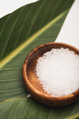 Close up view of sea salt in wooden bowl, and green leaves on white