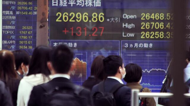 マスクをして出勤する日本人ビジネスマンと株価ボード電光掲示板