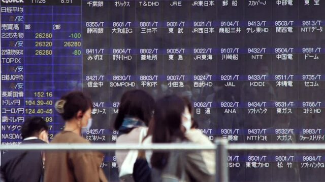 マスクをして出勤する日本人ビジネスマンと株価ボード電光掲示板