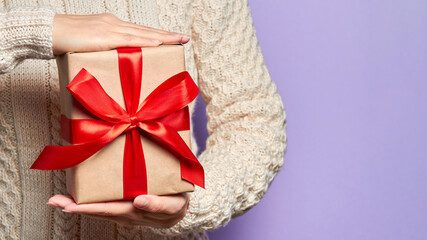 Girl holding a Christmas or New Year gift box with a red ribbon on a purple background