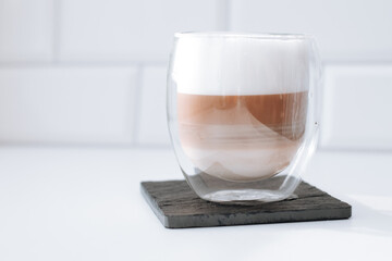 Cappuccino coffee in a double glass on a black slate board against white bricks wall background