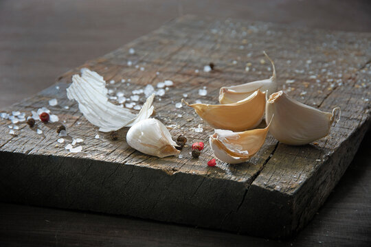 Still life with garlic cloves, coarse salt and peppercorns on a wooden board