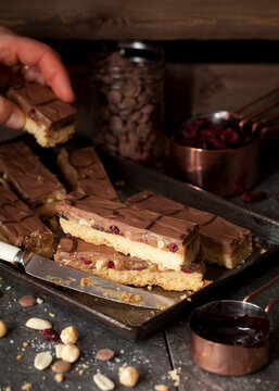 Person Taking A Slice of Millionaires Caramel Shortbread with Dried Fruit and Nuts