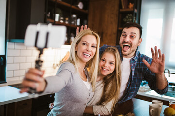 Girl and her beautiful parents are cutting vegetables and smiling while cooking in kitchen at home make selfie photo.