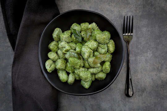 Spinach and basil gnocchi with sage in a black bowl on a grey surface