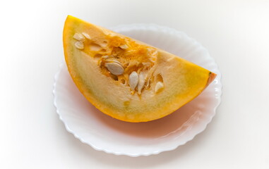 A piece of pumpkin in close-up on a white ceramic plate on a white background. Focus in the center