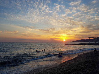 Fototapeta premium People sunbathing, have a party on the sandy tropical picturesque rocky beach during sunset