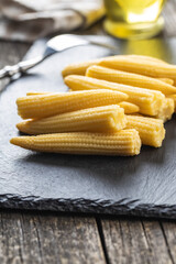 Pickled young baby corn cobs on black stone cutting board.