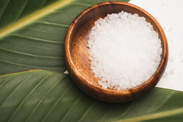Green leaves and wooden bowl with sea salt on white