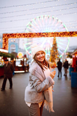 Obraz na płótnie Canvas Young woman with caramel apple on Christmas market. Smiling woman in winter style clothes posing at festive street market. Lights around. Winter holiday.