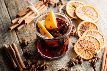 Mulled red wine with oranges and different spices in glass on the rustic background. Christmas food. Winter decorations. Selective focus. Shallow depth of field.
