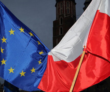 european union flag tied together with flag of Poland against evening sky and Saint Marys church in Krakow