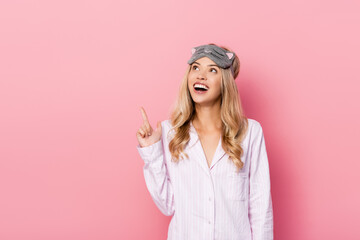  woman in blindfold and pajamas pointing with finger at pink background