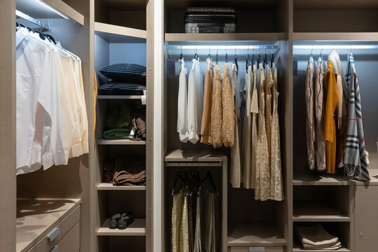 Modern wooden wardrobe with women clothes hanging on rail in walk in closet, Scandinavian style