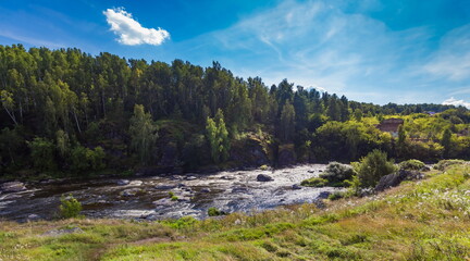 Fast river with rocky banks, overgrown with trees in summer