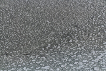 Stunning abstract view of sea ice that is partially frozen from above, aerial view with white icy sheets and blue, green ocean water below. 