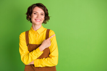 Photo of cheerful girl toothy smile direct finger empty space wear yellow shirt overall isolated green color background - Powered by Adobe