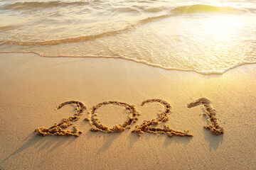 Fototapeta na wymiar Happy New Year 2021, lettering on sunrise beach with wave in the morning. Numbers 2021 year on the sea shore, message handwritten in the golden sand on beautiful beach background. New Years concept.