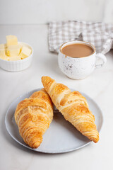 Fresh french croissants on plate, cup of coffee and milkman in the morning light. Continental morning breakfast on marble background.