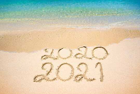 End of 2020 Happy New Year 2021, lettering on beach with wave and clear blue sea on sunny day. Handwritten inscription 2020 and 2021 on beautiful golden sand beach. New Years 2021 replace 2020 concept