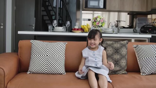 Cute little girl feel funny and laugh among using tablet for her relaxing at home 