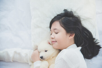 asian girl lying with siberian husky puppy on bed..