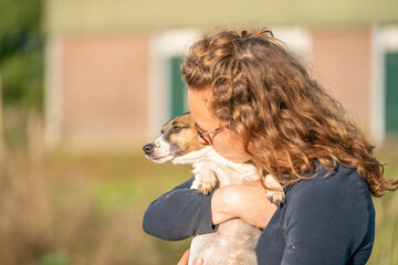 Farmer and her love for pets. Jack Russell Terrier dog lies in the womans arms. stable in background