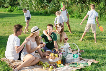 Portrait of adult people on picnic outdoors on background with kids playing active games