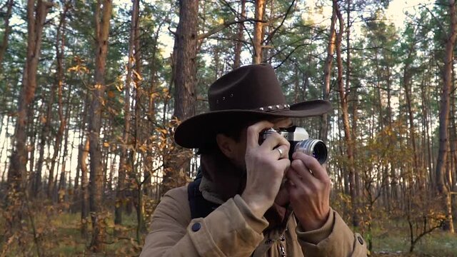 A man in a hat with a backpack takes pictures in the forest. Close-up. Travel concept. Slow motion
