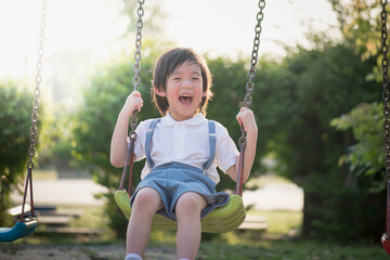 Cute Asian child having fun on swing in the park - obrazy, fototapety, plakaty