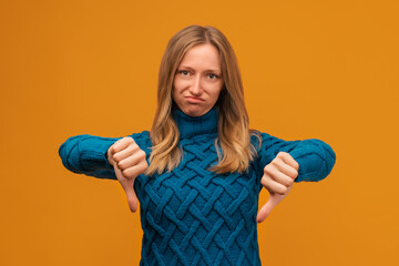 Unhappy Young woman showing a thumbs down. Unlike, dislike, failure gestures concept. Studio shot, yellow background