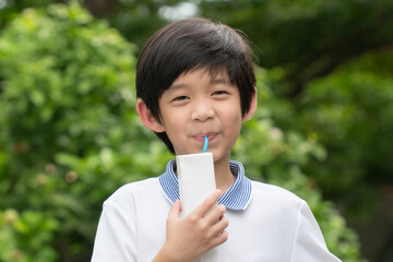 Cute Asian child  drinking a carton of milk from a box with a straw