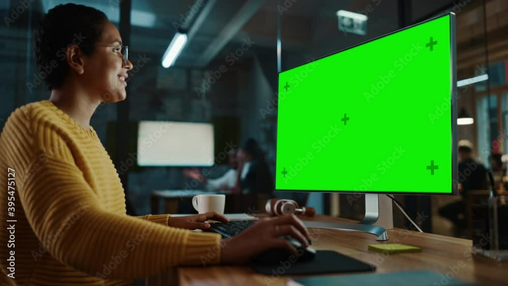 Poster Young Multiethnic Specialist Working on Desktop Computer with Green Screen Mock Up Display in Creative Office. Beautiful Diverse Female Manager with Short Hair and Glasses is Wearing a Yellow Jumper.