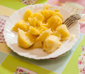 Sliced boiled potatoes with butter on a white plate and fork on the table