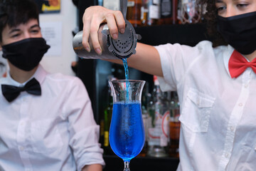 Unrecognizable waitress wearing protective face mask preparing cocktails in a pub. New normal in pubs.
