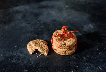 Shortbread cookies with pieces of chocolate are tied with red beautiful ribbon on a dark background. A place for text. View from above. New Year's cookies.