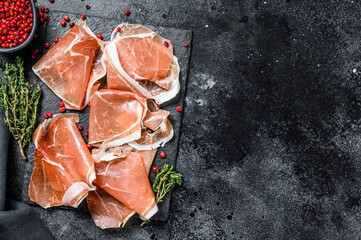 Italian prosciutto crudo with thyme, cured ham. Black background. Top view. Copy space