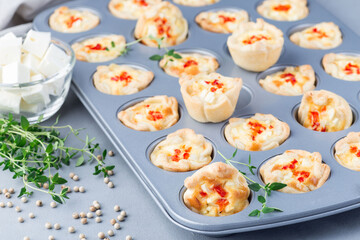 Mini quiche muffins with feta cheese, fried onion, thyme and red bell pepper, in a baking form, horizontal