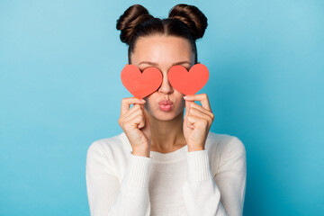 Photo of romantic girl hide eyes red paper hearts blow air kiss wear white sweater isolated blue color background