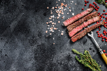 Grilled sliced rib eye steak with spices. BBQ beef. Black background. Top view. Copy space