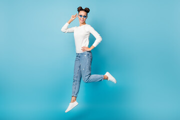 Fototapeta premium Full length photo of lady jump having fun wear sunglass white pullover jeans footwear isolated blue color background