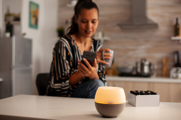 Woman watching video on phone and enjoying steam with essential oils from diffuser. Aroma health essence, welness aromatherapy home spa fragrance tranquil theraphy, therapeutic steam, mental health