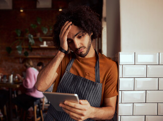 Young serious male cafe owner using digital tablet while standing leaning on wall